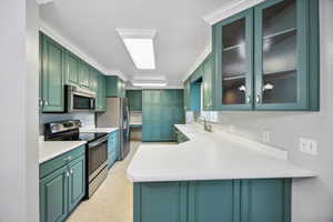 Kitchen featuring sink, stainless steel appliances, green cabinets, kitchen peninsula, and ornamental molding