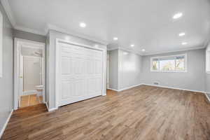 Promary bedroom featuring ensuite bathroom, light hardwood / wood-style flooring, a closet, and ornamental molding