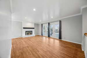 Unfurnished living room with hardwood / wood-style floors, french doors, crown molding, and a brick fireplace