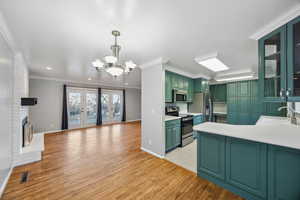 Kitchen featuring appliances with stainless steel finishes, a brick fireplace, sink, light hardwood / wood-style floors, and green cabinets