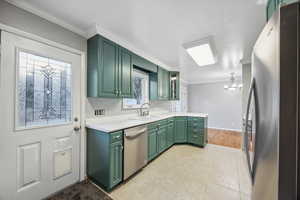 Kitchen featuring appliances with stainless steel finishes, ornamental molding, green cabinets, and sink