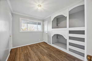 Interior space featuring built in shelves, dark hardwood / wood-style floors, and ornamental molding