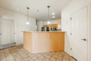 Kitchen featuring kitchen peninsula, light brown cabinets, stainless steel appliances, and decorative light fixtures