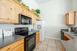 Kitchen with black appliances, light tile patterned flooring, sink, and light brown cabinets