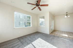 Carpeted spare room featuring ceiling fan with notable chandelier