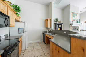 Kitchen featuring kitchen peninsula, sink, black appliances, a stone fireplace, and light tile patterned flooring