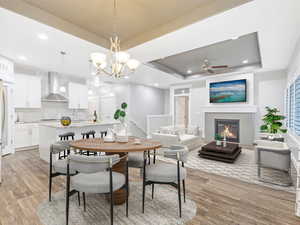 Dining area with a raised ceiling, sink, ceiling fan with notable chandelier, and light wood-type flooring