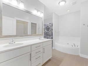 Bathroom with a washtub, vanity, stacked washing maching and dryer, and tile patterned flooring