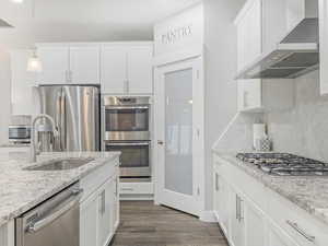 Kitchen featuring dark wood-type flooring, stainless steel appliances, wall chimney range hood, decorative light fixtures, and white cabinets