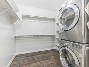 Clothes washing area with dark wood-type flooring and stacked washer / drying machine