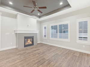 Unfurnished living room with hardwood / wood-style flooring, ceiling fan, a healthy amount of sunlight, and a tray ceiling