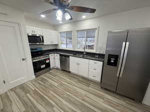 Kitchen featuring sink, decorative backsplash, ceiling fan, white cabinetry, and stainless steel appliances