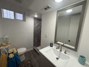 Bathroom featuring hardwood / wood-style floors, vanity, toilet, tiled shower, and a textured ceiling