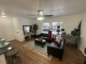 Living room with a textured ceiling, ceiling fan, and dark wood-type flooring