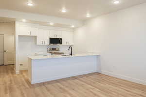 Kitchen with kitchen peninsula, light wood-type flooring, stainless steel appliances, and white cabinetry