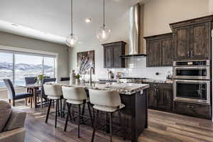 Kitchen featuring a mountain view, a center island with sink, wall chimney exhaust hood, and hardwood / wood-style flooring