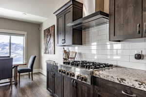 Kitchen with dark brown cabinetry, wall chimney range hood, stainless steel gas cooktop, tasteful backsplash, and dark hardwood / wood-style floors