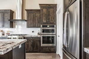 Kitchen with dark brown cabinets, stainless steel appliances, and wall chimney range hood