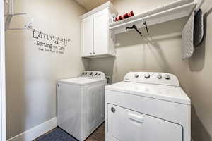 Clothes washing area featuring washer and clothes dryer, cabinets, and dark hardwood / wood-style floors