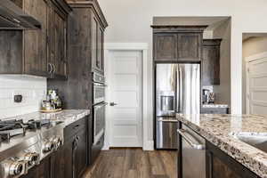 Kitchen featuring range hood, dark hardwood / wood-style flooring, light stone counters, dark brown cabinetry, and stainless steel appliances