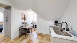 Kitchen featuring a textured ceiling, light stone counters, sink, and vaulted ceiling