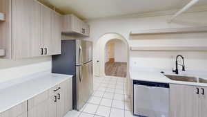 Kitchen with light tile patterned floors, light brown cabinetry, sink, and appliances with stainless steel finishes