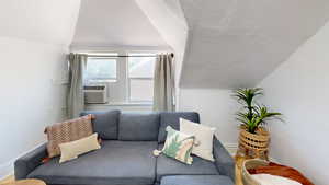 Living room with cooling unit, a textured ceiling, and vaulted ceiling