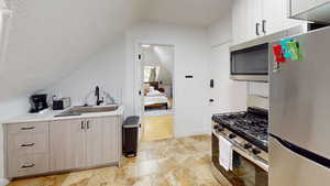 Kitchen with appliances with stainless steel finishes, light brown cabinets, vaulted ceiling, and sink