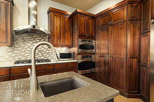 Kitchen featuring tasteful backsplash, light wood flooring,  exhaust hood, and appliances with stainless steel finishes and a hidden pantry.