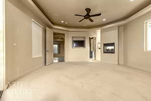 Primary bedroom featuring a raised ceiling, ceiling fan, and a multi sided fireplace