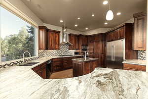 Kitchen featuring sink, appliances with stainless steel finishes, backsplash, decorative light fixtures, and wall chimney exhaust hood and textured marble countertops.