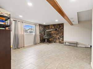 Unfurnished living room featuring beam ceiling and a wood stove