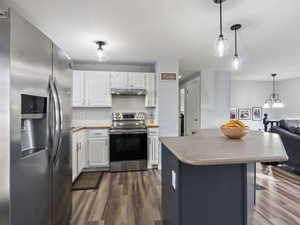 Kitchen featuring dark hardwood / wood-style flooring, white cabinetry, stainless steel appliances, and hanging light fixtures