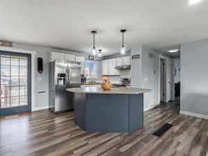 Kitchen with white cabinets, stainless steel appliances, hanging light fixtures, and dark hardwood / wood-style floors