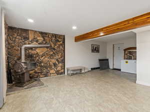 Unfurnished living room featuring beam ceiling and a wood stove