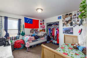 Carpeted bedroom featuring a textured ceiling and a closet