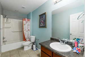 Full bathroom with a textured ceiling, vanity, shower / bathtub combination with curtain, tile patterned flooring, and toilet