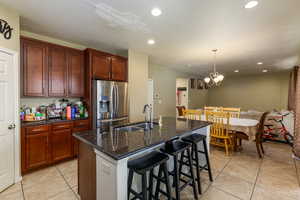 Kitchen with a kitchen island with sink, sink, a notable chandelier, stainless steel fridge with ice dispenser, and light tile patterned flooring