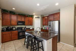 Kitchen featuring light tile patterned flooring, sink, an island with sink, and black appliances