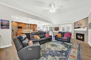 Living room featuring ceiling fan, light wood-type flooring, ornamental molding, and vaulted ceiling