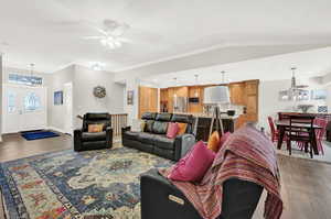 Living room with ceiling fan with notable chandelier, dark hardwood / wood-style flooring, lofted ceiling, and crown molding