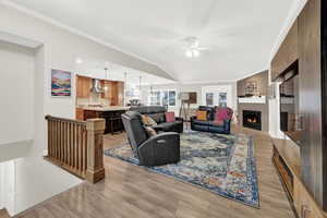 Living room with ceiling fan, ornamental molding, lofted ceiling, and light wood-type flooring