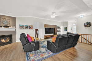 Living room with a tiled fireplace, ceiling fan, crown molding, and light hardwood / wood-style floors