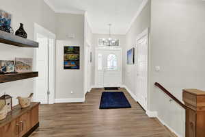 Entrance foyer featuring wood-type flooring, an inviting chandelier, and ornamental molding