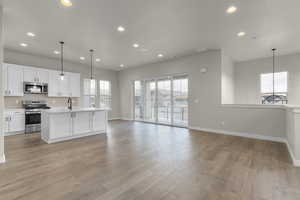 Kitchen featuring white cabinetry, stainless steel appliances, an island with sink, pendant lighting, and light hardwood / wood-style floors