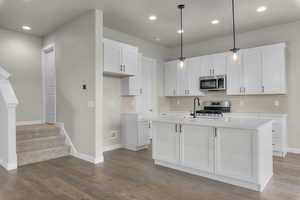 Kitchen with pendant lighting, stainless steel appliances, white cabinetry, and a kitchen island with sink