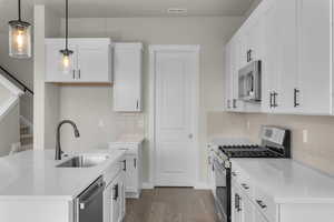 Kitchen with pendant lighting, white cabinets, sink, decorative backsplash, and stainless steel appliances