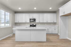 Kitchen with white cabinets, appliances with stainless steel finishes, light hardwood / wood-style floors, and an island with sink