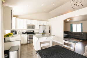 Kitchen with ceiling fan, dark hardwood / wood-style floors, vaulted ceiling, a kitchen island, and appliances with stainless steel finishes