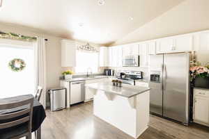 Kitchen with sink, a kitchen island, lofted ceiling, white cabinets, and appliances with stainless steel finishes